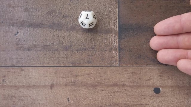 Hand roll a lucky number 7 on a 12 sides dice. Wooden background, flat lay, 4k.