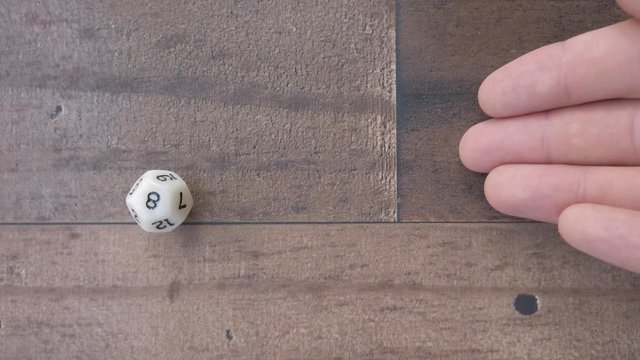Fingers roll a 12 sided dice and lands on a 8. 4k Flat lay, closeup shot.