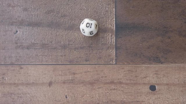 Twelve sided dice rolls and lands on a ten. on wood background. closeup.