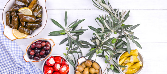 Traditional greek cuisine. Wrapped rice in grape leaves. Dolma with lemon, spices, various pickled olives and hot peppers. Fresh branches and homemade food.