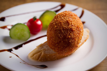 Chicken Kiev and vegetables on white plate, wooden background. Breaded chicken breast stuffed with herbs and butter