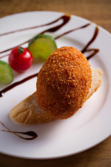 Chicken Kiev and vegetables on white plate, wooden background. Breaded chicken breast stuffed with herbs and butter