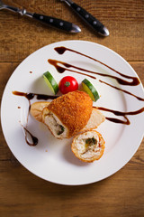 Chicken Kiev and vegetables on white plate, wooden background. Breaded chicken breast stuffed with herbs and butter