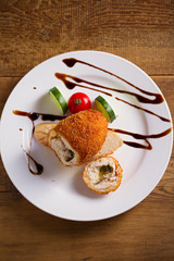 Chicken Kiev and vegetables on white plate, wooden background. Breaded chicken breast stuffed with herbs and butter
