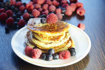 Pancakes with berries and maple syrup with raspberries and blueberries on a black background