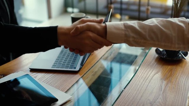 Close-up of the handshake of business partners in slow motion. There are laptops on the table. Business meeting was success. No faces