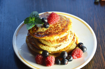 Pancakes with berries and maple syrup with raspberries and blueberries on a black background