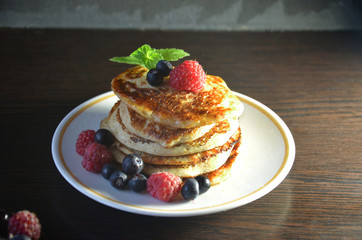 Pancakes with berries and maple syrup with raspberries and blueberries on a black background