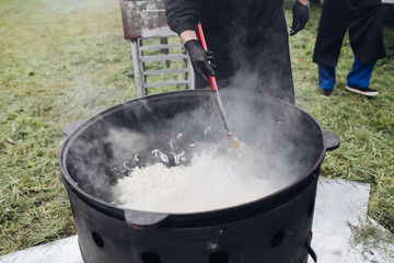 Process of cooking healthy onion in cauldron while having picnic. Cropped view of man in black...