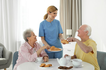 Nurse assisting while elderly people having breakfast at retirement home