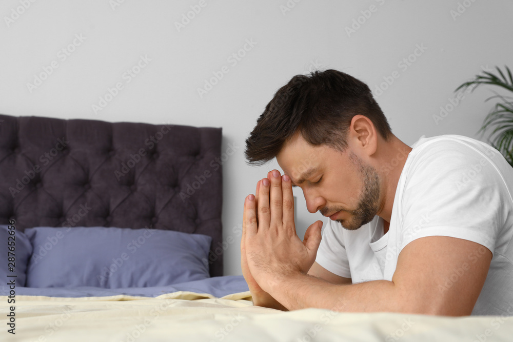 Wall mural Handsome man saying bedtime prayer at home. Space for text