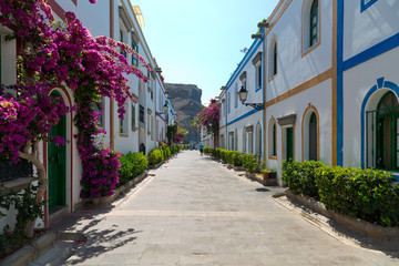Fototapeta na wymiar Street with white houses and colorful flowers, small fishing village. Romantic architecture of the port of Mogan in Gran Canaria, Spain.