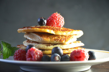 Pancakes with berries and maple syrup with raspberries and blueberries on a black background