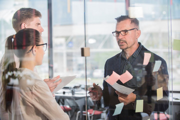 Happy office workers smiling while female colleague writing ideas on   sticky notes during meeting, group of successful cheerful employees   enjoying working process, collaboration and brainstorming f