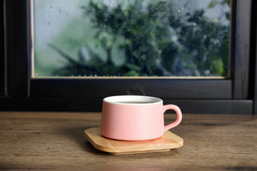 Cup of hot drink on window sill against glass with rain drops, space for text