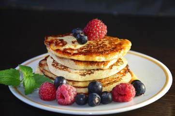 Pancakes with berries and maple syrup with raspberries and blueberries on a black background