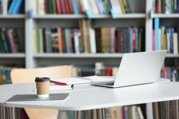 Laptop, drink and stationery on table in library