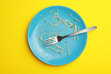Dirty plate with food leftovers and fork on yellow background, top view