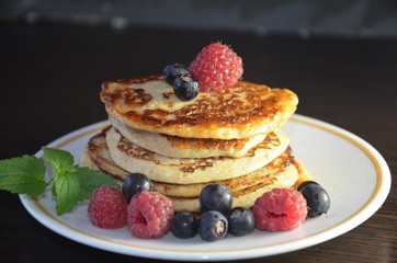 Pancakes with berries and maple syrup with raspberries and blueberries on a black background