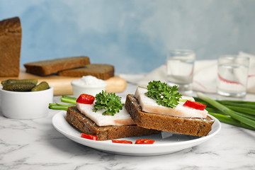 Composition with plate of pork fatback sandwiches on marble table against blue background