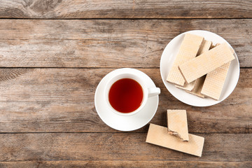 Delicious wafers with cup of tea on brown wooden background, top view. Space for text
