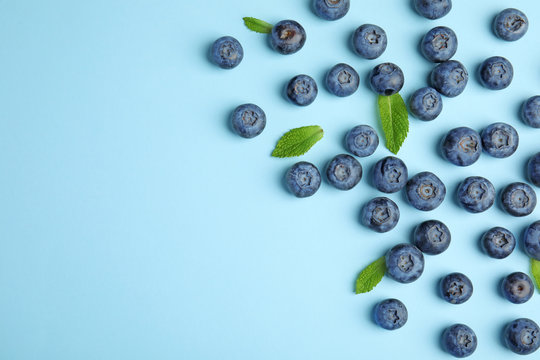Tasty ripe blueberries and leaves on blue background, flat lay with space for text