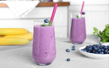 Glasses of delicious blueberry smoothie on light marble table in kitchen