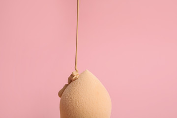 Liquid foundation pouring on makeup sponge against pink background