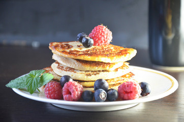 Pancakes with berries and maple syrup with raspberries and blueberries on a black background
