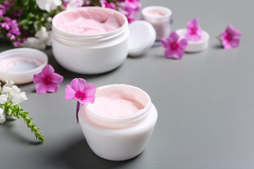 Jars of body cream and flowers on grey background