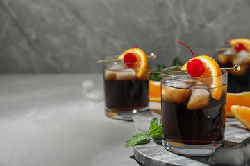 Glass of delicious cocktail decorated with cherry and orange on light grey table. Space for text