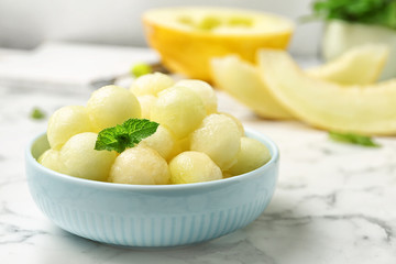 Plate of melon balls with mint on white marble table, closeup