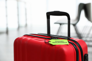 Red suitcase with TRAVEL INSURANCE label indoors, closeup