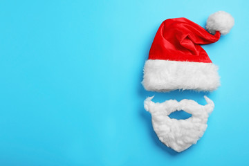 Obraz na płótnie Canvas Santa Claus hat and beard on light blue background, flat lay. Space for text