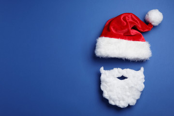 Santa Claus hat and beard on blue background, flat lay. Space for text