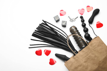 Paper shopping bag with different sex toys on white background, top view