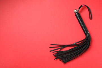Black whip on red background, top view with space for text. Sexual role play accessory