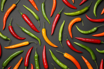 Different colorful chili peppers on black background, flat lay
