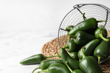 Green chili peppers and metal basket on marble table. Space for text