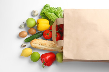 Paper bag with different groceries on white background, top view