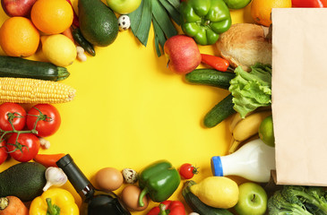 Paper bag with different groceries on yellow background, flat lay. Space for text