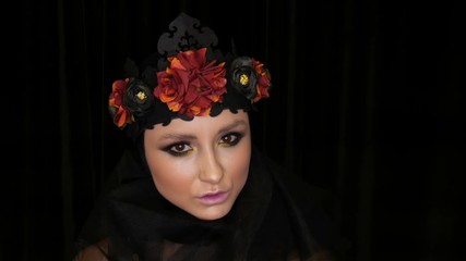 Professional girl model with beautiful makeup poses in a black cap and wreath on her head in front of the camera on a black background in the image of a black widow. High-fashion