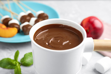 Fondue pot with milk chocolate on light table, closeup