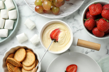 Dipping strawberry into fondue pot with white chocolate on marble table, top view