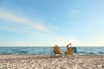 Fototapeta na wymiar Young couple relaxing in deck chairs on beach near sea