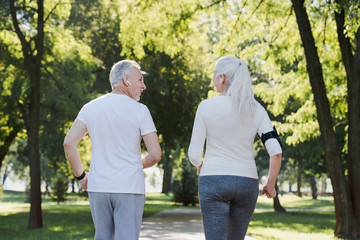Close up back view of healthy mature couple jogging in park at early morning