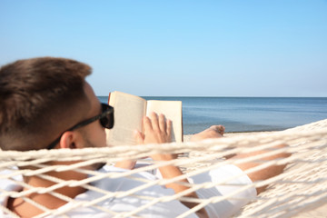 Young man reading book in hammock on beach