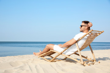 Young man relaxing in deck chair on sandy beach