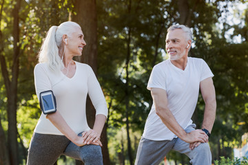 Low angle view of smiling senior couple doing warm up exercises while standing in park outdoors and...
