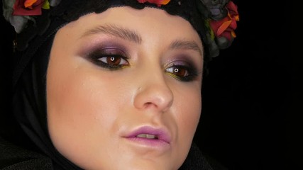 Professional girl model with beautiful makeup poses in a black cap and wreath on her head in front of the camera on a black background in the image of a black widow. High-fashion